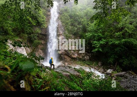 Rückansicht der Frau, die auf einem Felsen am Wasserfall im Wald steht Stockfoto