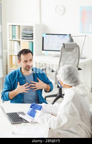 Reifer Mann sitzt gegenüber dem Arzt und zeigt auf seine Lungen er beklagt Schmerzen in den Lungen im Krankenhaus Stockfoto