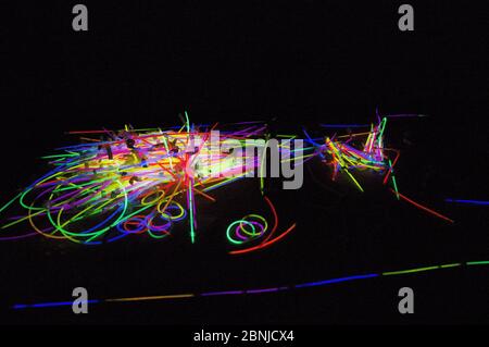 Ein Haufen Glühstäbchen im Dunkeln mit leuchtenden neonfarbenen Glühstäbchen gerade und geschwungene Formen Stockfoto