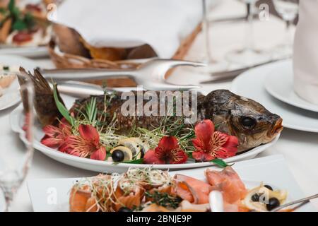 Gefüllte Fische in Blumen, Zitrone, roter Pfeffer. Fragment der Tabelleneinstellung Stockfoto