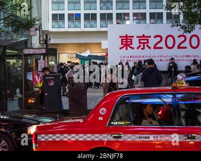 Shibuya, Japan - 7.2.20: Ein rotes Taxi, das vor Leuten vorbeifährt, die in Shibuya auf die Überquerung warten Stockfoto