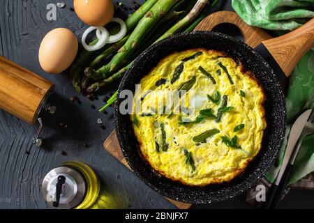 Gesundes Spargelomelett. Omelette mit Spargel und Zwiebeln in einer Gusseisenpfanne auf einer Steinplatte. Draufsicht flach legen Hintergrund. Stockfoto