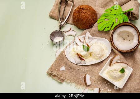 Laktosefreies Kokoseis. Spezieller Löffel, Hälften von Obst, Flocken. Veganes Dessert-Konzept. Hellgrüner Hintergrund, Draufsicht Stockfoto