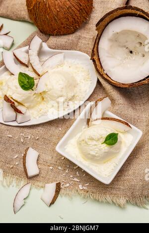 Laktosefreies Kokoseis. Spezieller Löffel, Hälften von Obst, Flocken. Veganes Dessert-Konzept. Hellgrüner Hintergrund Stockfoto