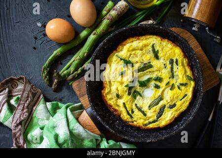 Gesundes Spargelomelett. Omelette mit Spargel und Zwiebeln in einer Gusseisenpfanne auf einer Steinplatte. Draufsicht flach legen Hintergrund. Stockfoto