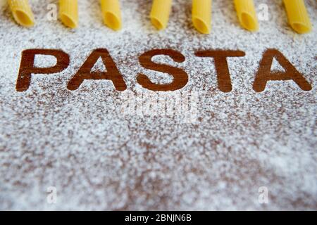 Holzhintergrund mit bestreut Mehl und das Wort Pasta geschrieben. Selektiver Fokus Stockfoto