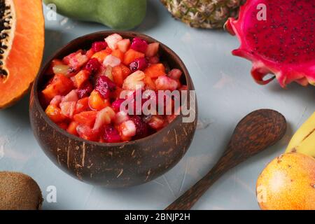 Tropischer Obstsalat in Kokosnussschale auf hellblauem Hintergrund, Nahaufnahme, Horizontal Format Stockfoto