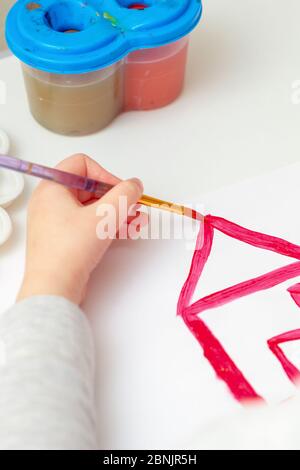 Nahaufnahme der Hand des Kindes, das ein Hausdach auf weißem Papier zeichnet. Konzept des kreativen Lernens. Stockfoto