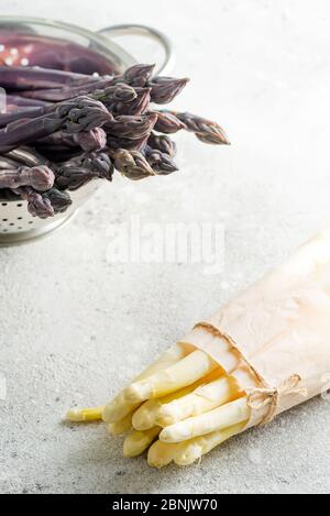 Roher Bio-Spargel lila Speere in Sieb und Bund von weißem Spargel als gesunde Ernährung Lebensmittel auf einem hellen Stein Hintergrund. Stockfoto