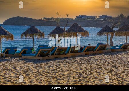 Golden Hour luxuriöse Holzliegen mit blauer Matratze & Bambus Sonnenschutz Sonnenschirme am leeren Sandstrand am Mykonos, Griechenland Paradise Beach. Stockfoto