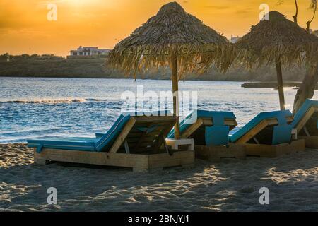 Golden Hour luxuriöse Holzliegen mit blauer Matratze & Bambus Sonnenschutz Sonnenschirme am leeren Sandstrand am Mykonos, Griechenland Paradise Beach. Stockfoto