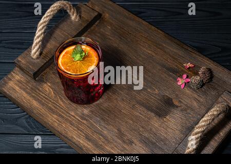 Leuchtend roter Old Fashioned Cocktail mit Whiskey auf einem Holzbrett. Verziert mit Zapfen und kleinen rosa Blüten. Perfektes Beispiel für eine Bedienung Stockfoto