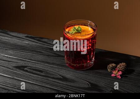Altmodischer klassischer Cocktail mit Orange in Kristallglas auf einem Holztisch in der Nähe von Zapfen und kleinen rosa Blume Stockfoto
