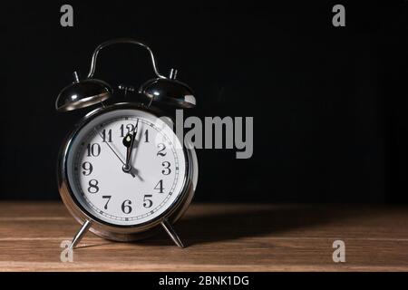 Antike Wecker Vintage mit Glocke metallic auf einem Holztisch und schwarzem Hintergrund Nahaufnahme in Mitternacht Stockfoto