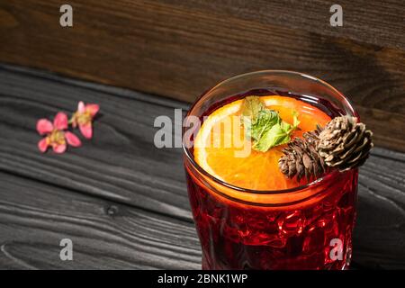 Frischer Cocktail mit Orange, Minze und Eis, verziert mit Zapfen auf einem Holztisch mit rosa Blumen Stockfoto