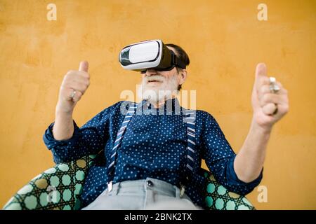 Portrait von zufriedenen glücklichen alten Mann mit gepflegten Bart zeigt seine Daumen nach oben, während mit Virtual-Reality-Brille für das Ansehen von Film. Studioaufnahme Stockfoto