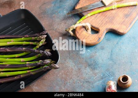 Frisches natürliches Bio-grünes und violettes Spargelgemüse in einer Pfanne, die bereit ist, gesunde Lebensmittel auf einem Steinhintergrund zu kochen. Stockfoto