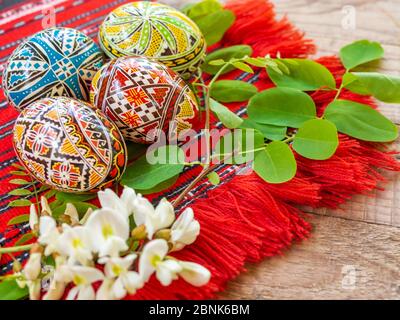 Schön handverzierte rumänische orthodoxe ostereier mit traditionellen Motiven auf einem roten Tuch mit Akazienblumen beiseite Stockfoto