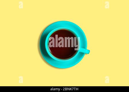 Blaue Tasse mit Tee auf gelbem Hintergrund. Duftender heißer Tee. Aussicht von oben, minimalistisch. Stockfoto