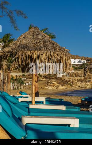 Leere luxuriöse Holzliegen mit blauer Matratze und Bambus Sonnenschirmen am Sandstrand von Mykonos, Griechenland Paradise Beach. Stockfoto