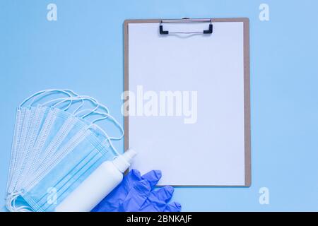 Medizinische Maske, Handschuhe und Handdesinfektionsmittel zum Schutz vor Infektionen und leere Zwischenablage mit leerem Papier auf blauem Hintergrund. Mock-up. Draufsicht. Flach Stockfoto