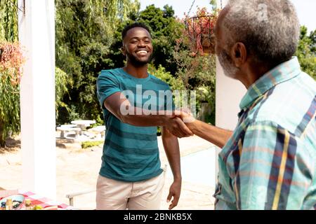 Älterer afroamerikanischer Mann, der bei einem Familienessen im Garten die Hände mit seinem Sohn hält Stockfoto