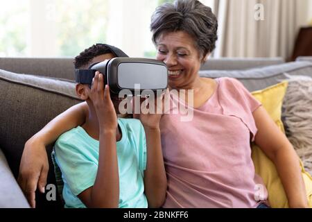 Ältere Mischrassenfrau und ihr Enkel zu Hause mit VR-Headset Stockfoto