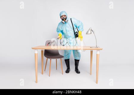 In voller Länge Foto von professionellen Reiniger Mann in Bio weiß Gefahr waschen desinfizieren Büro Schreibtisch verwenden Sprayer Ausrüstung isoliert über grauen Hintergrund Stockfoto