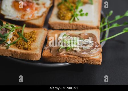 Verschiedene Sandwiches zum Frühstück, Snack, Vorspeisen mit Spiegelei, Erdnusspaste, Erbsenmikro. Flacher Lay. Dunkler Hintergrund. Schnell gesund Stockfoto