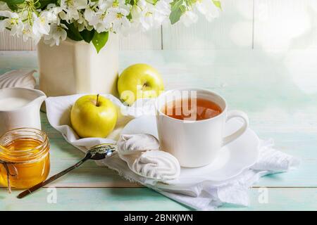 Tasse Tee mit Marshmallows, Honig und gelben Äpfeln und Ästen von Apfelbäumen in Vase auf Holztisch. Apple Urlaub. Apple Day. Teestunde. Sel Stockfoto
