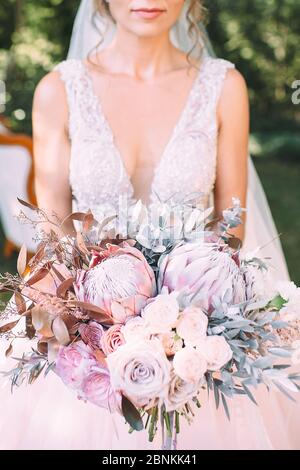 Nahaufnahme des Straußes einer Braut aus Rosen, Nelken, Proteas und silbernen Blättern in weißen, rosa, violetten, lavendelfarbenen Tönen. Die Braut hält einen Strauß in sich Stockfoto