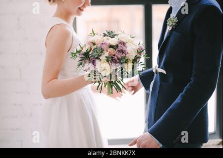 Nahaufnahme des Straußes einer Braut aus Rosen, Nelken, Sukkulenten in weißen, rosa, violetten, lavendelfarbenen Tönen. Die Braut in einem weißen Spitzenkleid hält eine Bouque Stockfoto