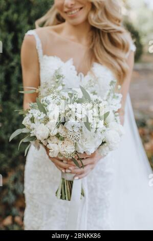 Nahaufnahme des Straußes einer Braut aus weißen Blumen. Die Braut in einem weißen Spitzenkleid hält einen Strauß in den Händen Stockfoto