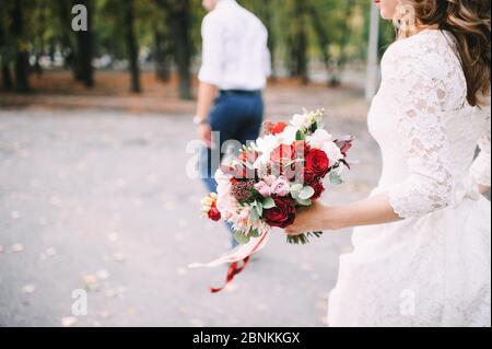 Brautstrauß aus nächster Nähe, das Bouquet besteht aus roten und weißen Rosen und Eukalyptus. Die Braut hält den Strauß Stockfoto