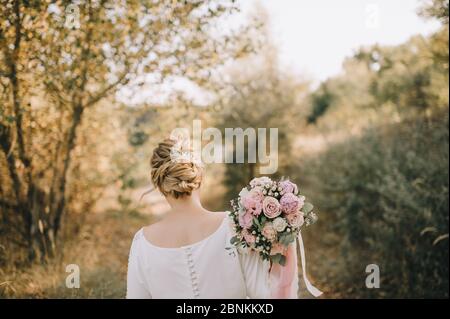 Nahaufnahme des Bouquets einer Braut aus Pfingstrosen, Rosen, Eukalyptus in weiß-rosa Schattierungen, die mit rosa Bändern gebunden sind. Die Braut hält einen Strauß in der Hand Stockfoto
