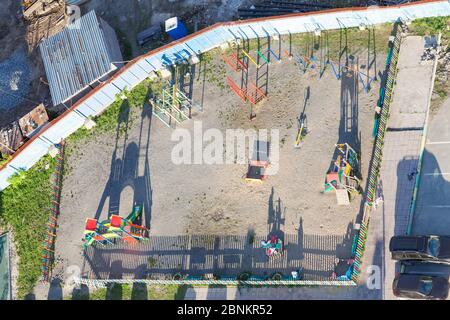 Draufsicht aus dem Fenster eines Mehrfamilienhauses auf einem Kinderspielplatz mit bunten Karussells mit einem Betonzaun in der Nähe des Gebäudes eingezäunt Stockfoto