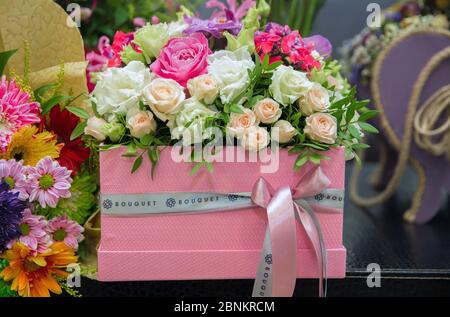 Der Strauß wird mit Band gebunden. Mehrfarbige Blumenstrauß . Ein Blumenstrauß in einer rosa Schachtel. Stockfoto
