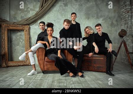 Gruppe von gemischten Rennen junge Menschen Blick auf die Kamera, während in einem schönen Loft sitzen. Kopierraum, Freundschaft, grauer Hintergrund. Stockfoto
