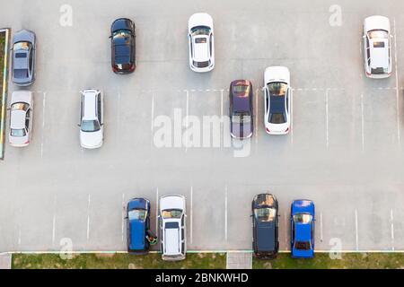 Draufsicht auf einen halbleeren Asphalt Parkplatz mit schwarz-weißen und blauen Autos in der Nähe eines Wohnhauses an einem Sommertag geparkt. Stockfoto