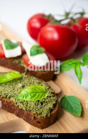 Traditionelle italienische Caprese Bruschetta: Sandwich Toast mit Basilikum Pesto Sauce, Mozzarella Käse und Tomaten auf dem Holzbrett von Basilikum l umgeben Stockfoto