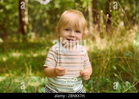 Porträt eines niedlichen Kleinkind Jungen in einem Feld zwischen dem Gras bei Sonnenuntergang. Ein Kind geht im Park spazieren. Im Freien. Happy Summer und Lifestyle Konzept. Kind Stockfoto