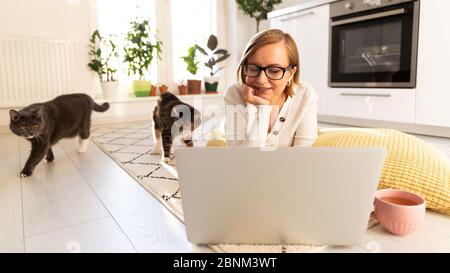 Freiberufliche Frau liegt im Wohnzimmer auf dem Teppich, Webinar ansehen. Hündin mit zwei Katzen im Gespräch durch Video-Chat mit ihrer Familie, die in Isolation du sind Stockfoto