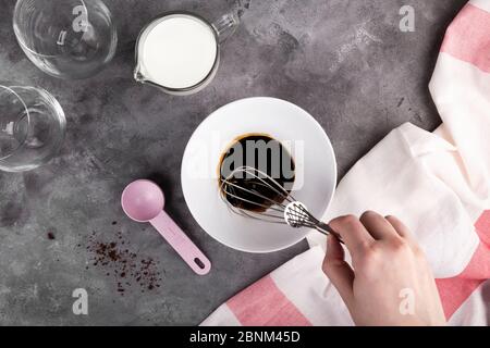 Kochen beliebten koreanischen Dalgon Kaffee Schritt für Schritt. Schritt 4 beginnt, löslichen Kaffee, Zucker und heißes Wasser mit Schneebesen in der Schüssel auf dunkelgrauen Backgrou schlagen Stockfoto