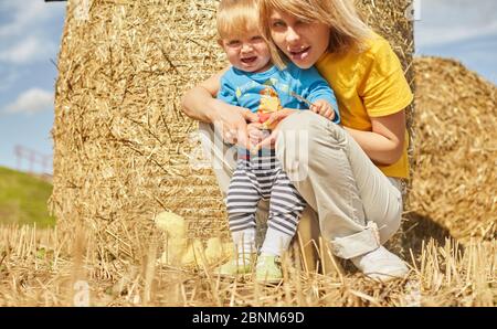 Frühling Porträt eines niedlichen Kleinkind Jungen mit Bär Spielzeug in einem Feld zwischen den trockenen Ohren und Gras, Heupyramide und Stroh. Im Freien. Schönen Sommer und Stockfoto