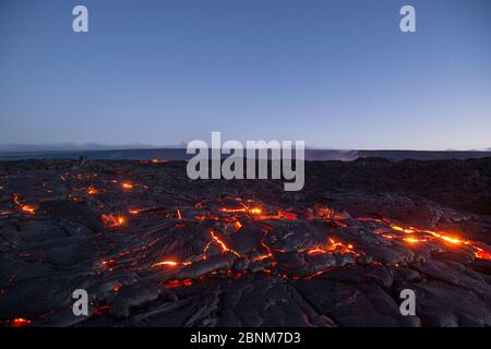 Heiße Lava leuchtet durch die Risse von Pahoehoe im 61G-Strömungsfeld, die von Pu'U O'o auf dem Kilauea Vulkan ausgeht und in Hawai zum Ozean fließt Stockfoto