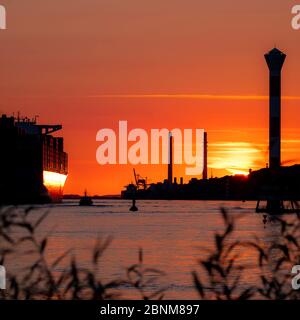 Sonnenuntergang über der Hamburger Elbe mit einem großen Containerschiff. Stockfoto