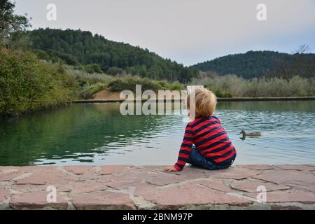 Blonde junge beobachten das Wasser Floß mit Enten, Farben der Natur Stockfoto