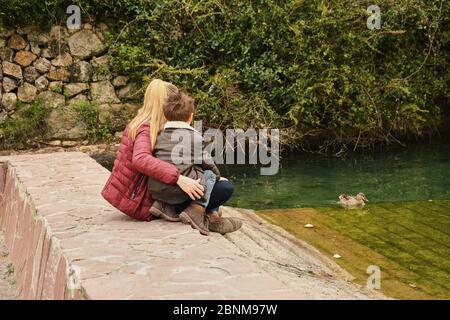 Mutter und Sohn beobachten das Wasserfloß mit Enten. Farben der Natur Stockfoto