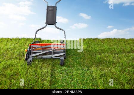 Rasenmähen von Hand. Symbolisches Foto, Spindelmäher auf Rasen gegen hellblau, Himmel Stockfoto