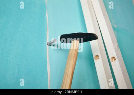 DIY Wandgestaltung 02, Schritt-für-Schritt Do-it-yourself Produktion, verschiedene türkisfarbene Flächen durch weiße Holzleisten getrennt, Schritt 11: Hammer in ein Dübel in das Loch in der Wand, um die Streifen zu befestigen Stockfoto